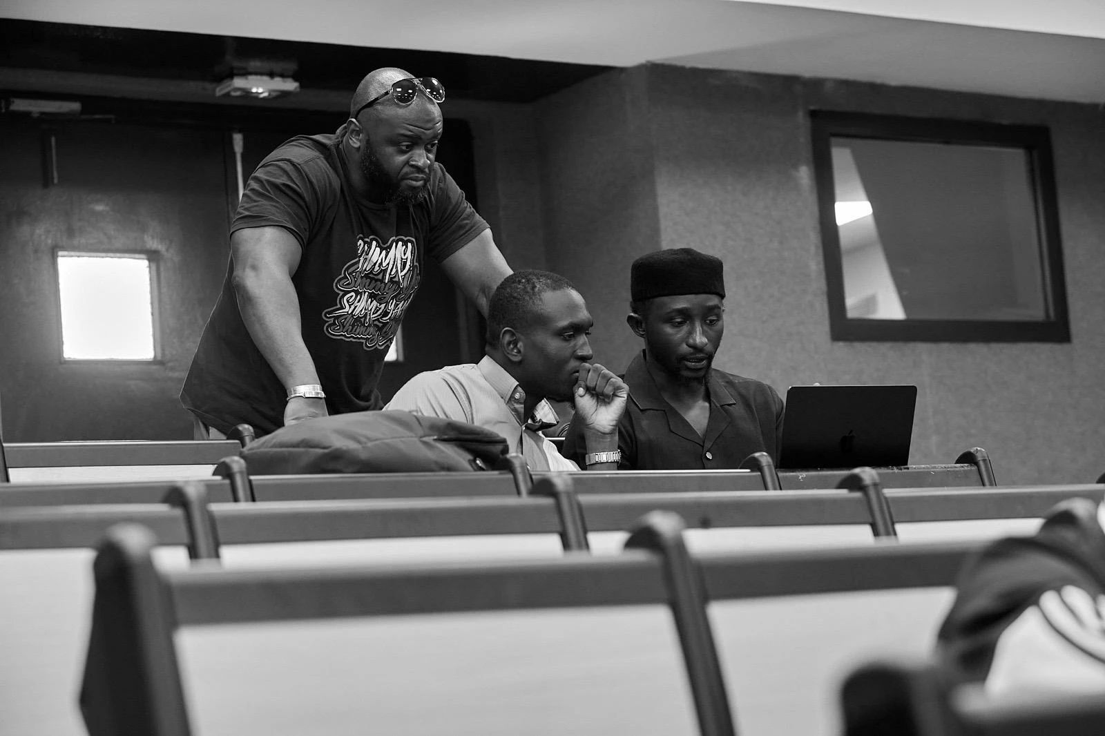 Trois hommes regardent ensemble l’écran d’un ordinateur, dans un amphithéâtre.